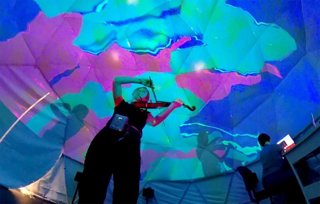 a violinist inside a projection dome looking at a data visualization presentation