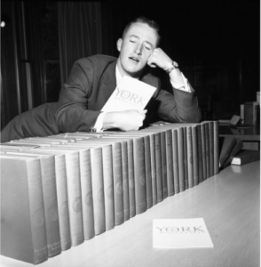 Image of student leaning on a row of books with a York University booklet in his hand