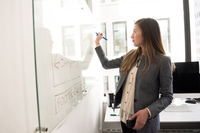 An image of a woman writing on dry-erase board