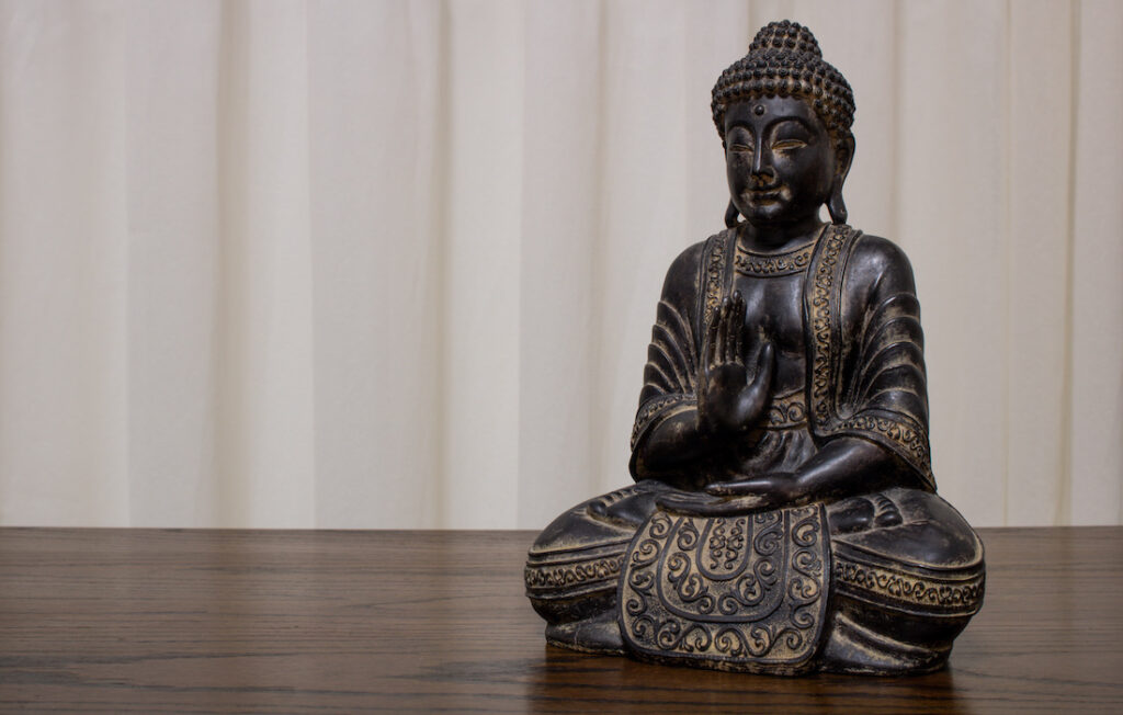 dusty buddha statue sitting in meditation on wooden table