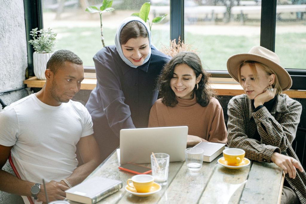 four people sit at a table around a laptop