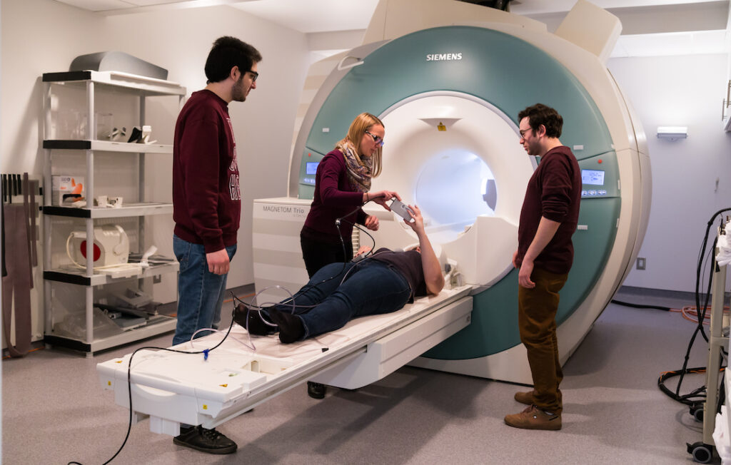 three people assist a woman lying on a CT Scanner bed