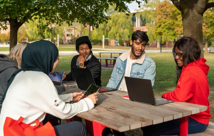 students sitting at a table talking under a tree