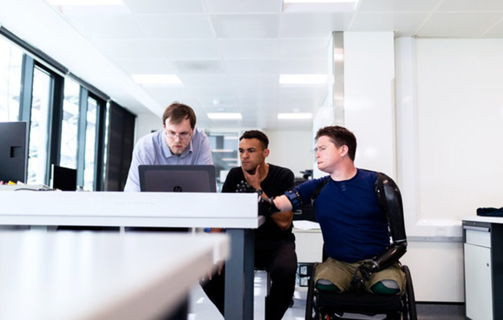 three men talking while looking at a laptop screen