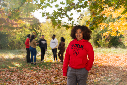 Photo of a student wearing a red York hoodie outdoors on campus during fall