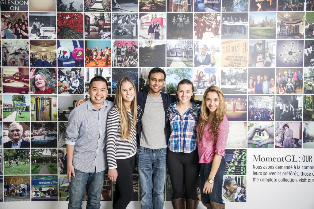 Five smiling students stand arm in arm in front of a collage wall filled with photos from campus life at Glendon College, representing community, diversity, and shared university experiences.