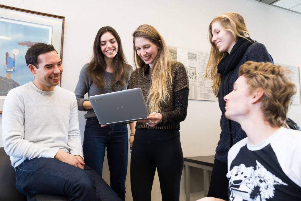 A group of students looking at a laptop and smiling
