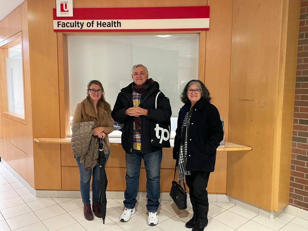 Three people standing together, smiling, below a sign saying: Faculty of Health