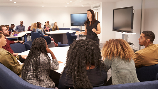 Woman stands in front of class during seminar while students raise hands