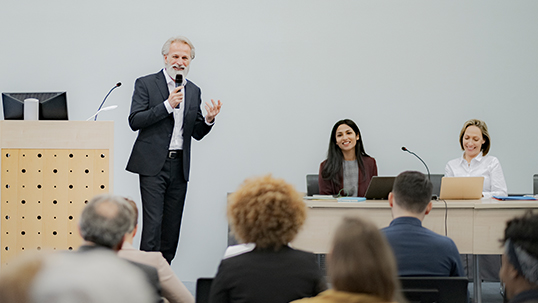 focused image of a speaker standing and speaking during a panel discussion