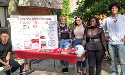 five students beside a stall with a banner of sociology undergraduate student association