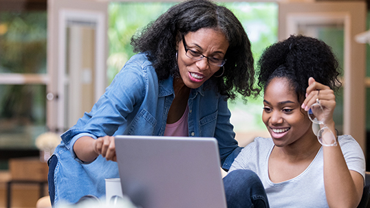 mother helps her daughter with some work on a computer