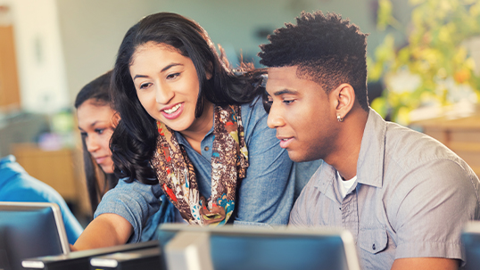 female staff member helps male student with a problem on his laptop.