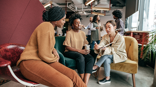 three female students work together on a project while seated down in a modern open office space