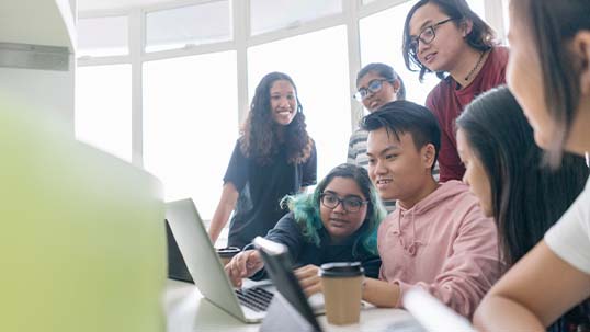 group of students huddle around a laptop