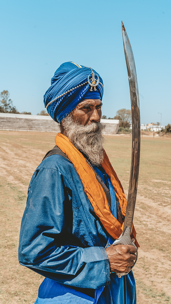A Sikh man in traditional attire, holding a long kirpaan