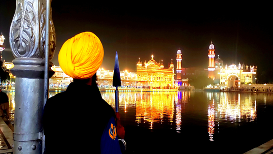 Sikh man in yellow turban looking at a gurdwara at night