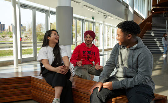 3 students, one wearing a york red hoodie, chatting and laughing