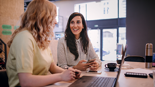 two female students smiling sitting in front of laptop