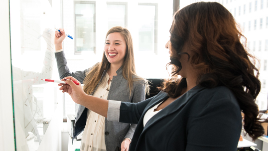 two young professional women writing on white board