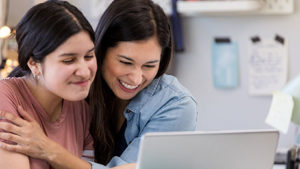 two female students smiling happily in front of laptop