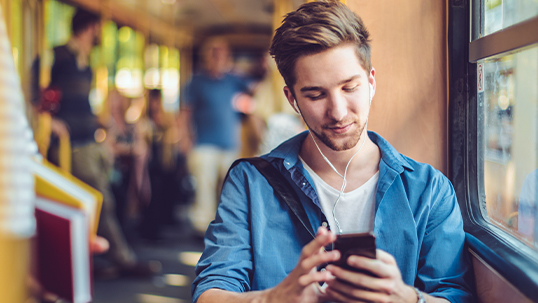 young male student using his phone and listening to music in ear buds