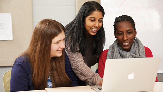 three young women using Apple laptop