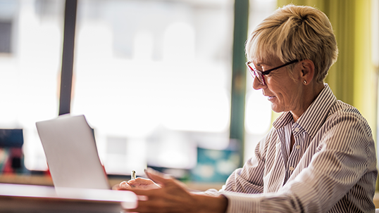 Older woman writes on laptop in her office