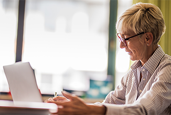Older woman writes on laptop in her office