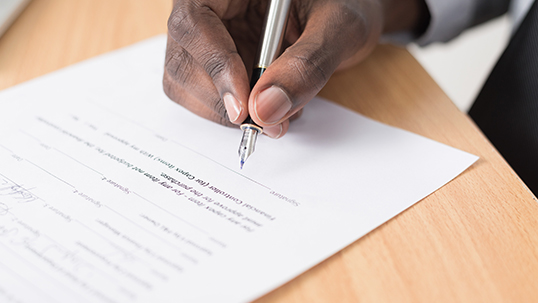 A hand hovers over a document holding a pen.