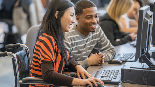 Two students at a computer, watching something and smiling