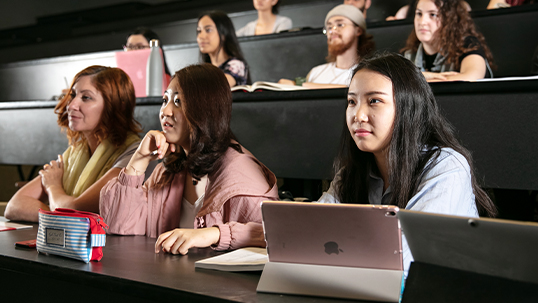 Group of students sit in front row of lecture hall during class