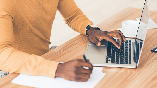 Young man uses laptop computer while writing notes