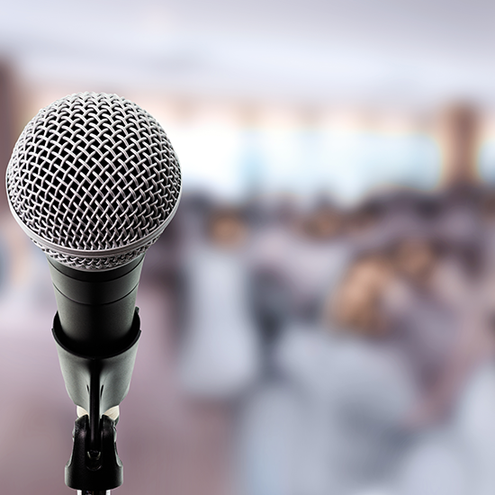 Image of a microphone with attendees in the background 