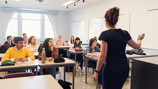 rear view of a woman addressing a class while the students sit and listen