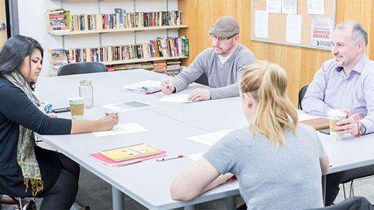 Men and women seated at large desk drinking coffee and reviewing study notes