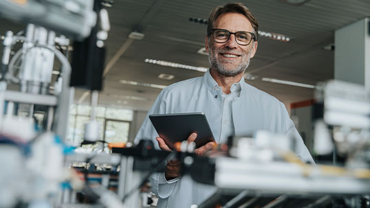 man smiles while holding tablet and standing in science lab