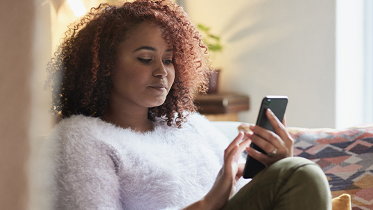 Black female woman scrolling on her phone while seated on a couch