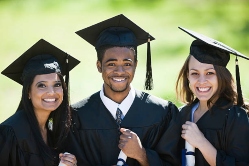 Two female and one male with big smiles wearing cap and gown on graduation day
