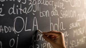 hand holds chalk while writing words in several languages on chalkboard