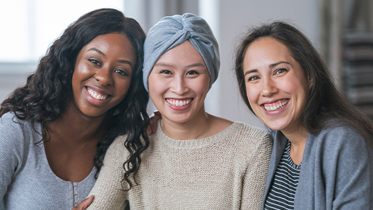 Three racially diverse women are sitting, posing, and smiling at the camera.