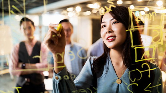 young east asian professional woman writing on transparent marker board in planning meeting