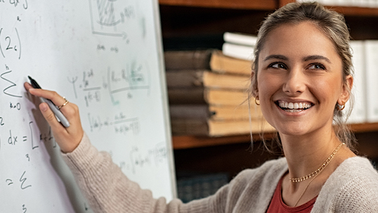 young woman smiles while writing algebraic equation on whiteboard