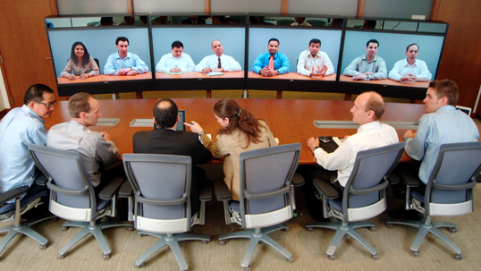 A group of HR workers have a virtual conference call with another group of workers in a boardroom.