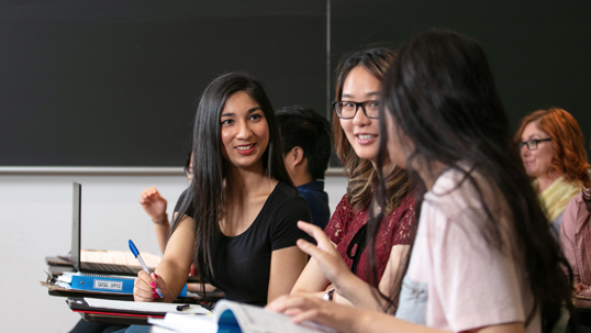 Three students are seated in a classroom and participating in a lecture.