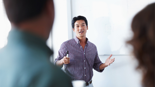 A male graduate student gives a presentation to two attentive listeners. 