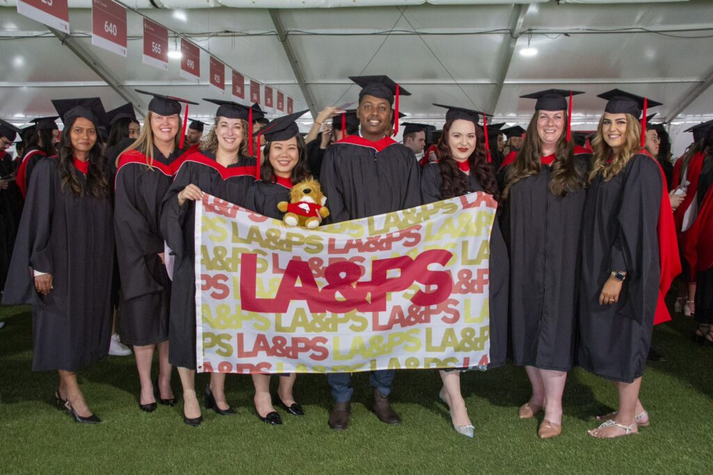 Eight graduates pose with the LA&PS flag