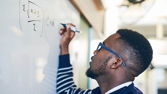 Black man looks upward while writing equation in marker on whiteboard