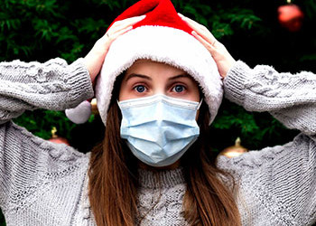 female with a mask and santa hat holding her head with hands