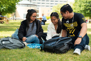 three york u students sitting outside on campus on sunny summer day